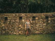 Man stands against an ancient stone wall.