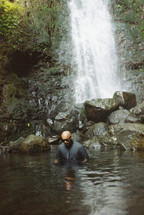 man wading in a water hole and waterfall 