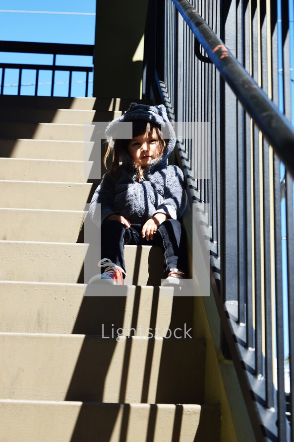 a toddler girl sitting on steps waiting 