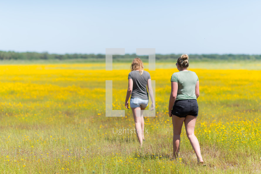 teen girls walking through a field of yellow flowers 