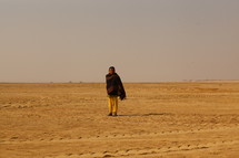 man standing in a desert wrapped in a blanket 