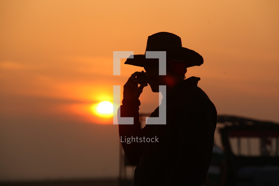 silhouette of a cowboy on a cellphone at sunset 