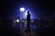 man standing on a dock at night in a fishing village 