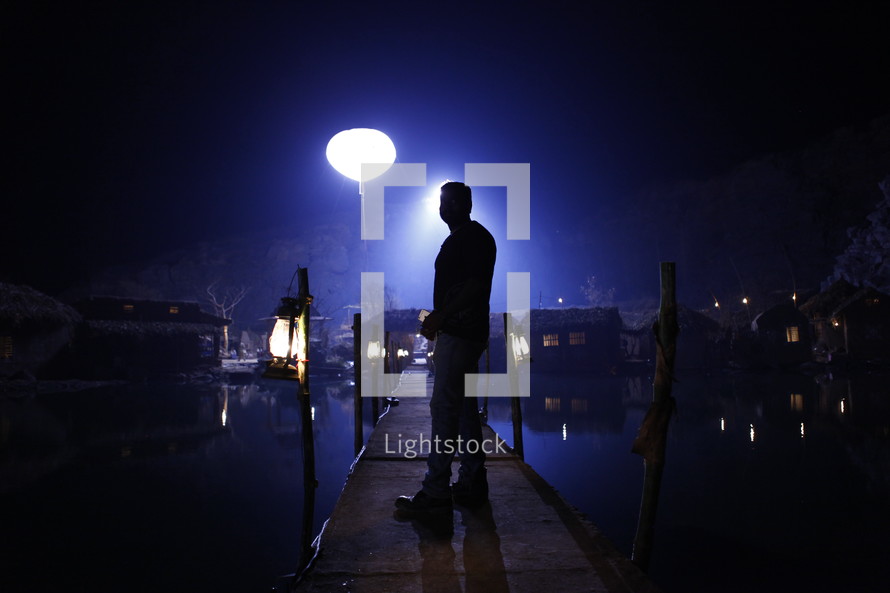 man standing on a dock at night in a fishing village 