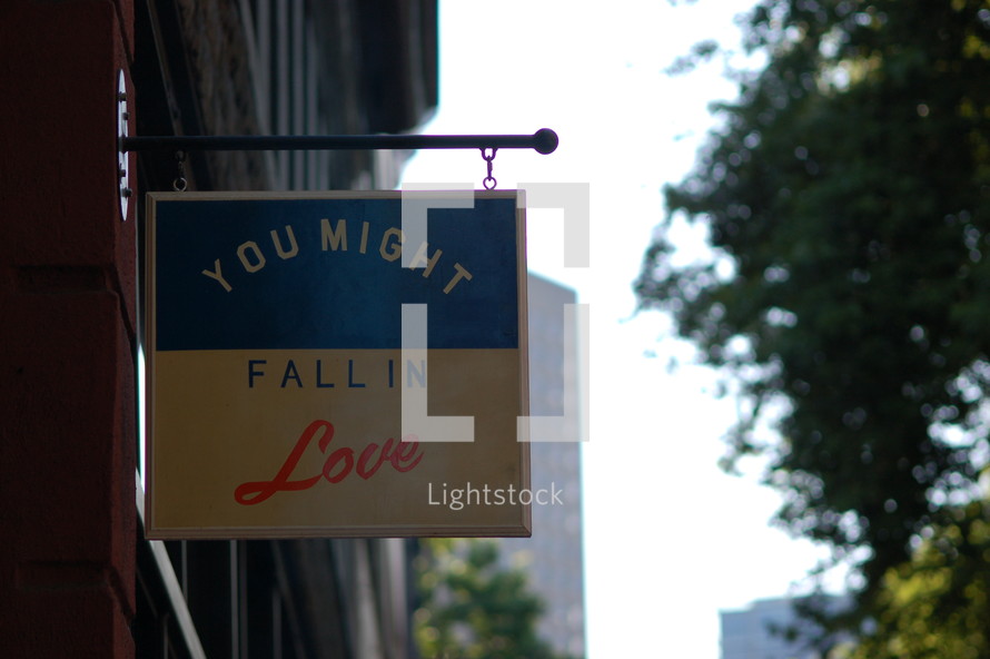 A sign hanging from a building that says, "You might fall in love."