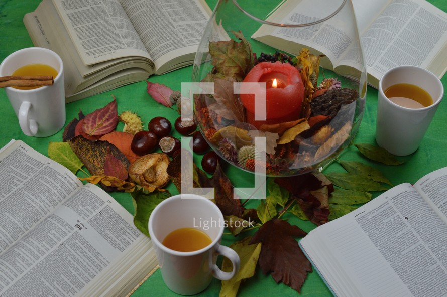 apple cider, open Bible, candle, and fall leaves on a green background 