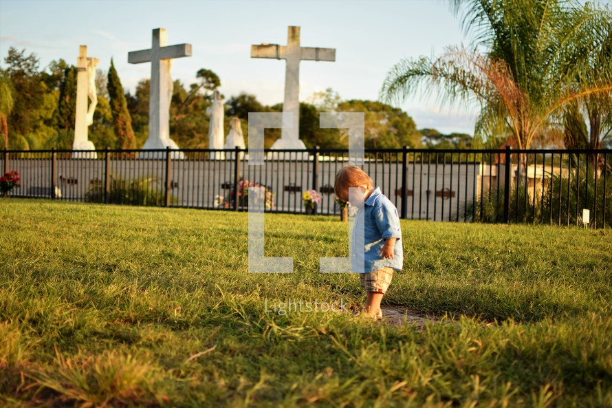 a toddler boy walking in the grass near crosses and statues 