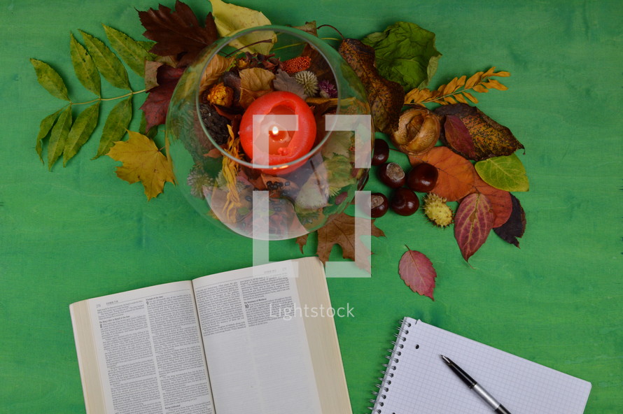 notebook, open Bible, pen, candle, and fall leaves 