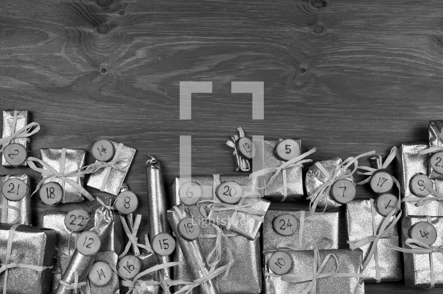 Border of advent calendar with twenty four silver presents on grey wood with negative space above