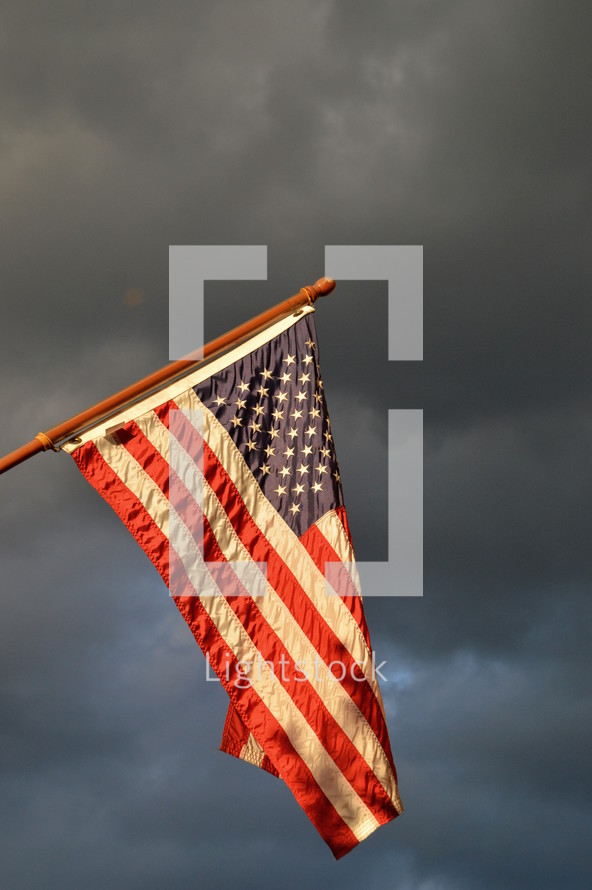 american flag hoisted up on flagpole in front of dark rainy cloudy sky while a storm is brewing