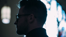 side profile of a man in glasses standing in a church 
