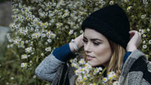 a woman standing in a field of wildflowers putting on a wool cap 