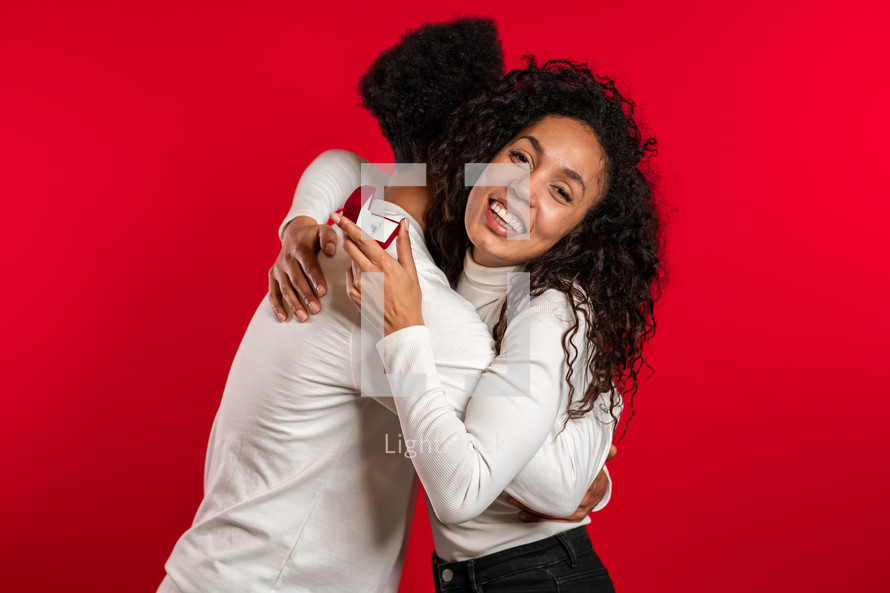 Young couple. African man makes marriage proposal to his lover woman with ring on red studio background. Love, holidays, happiness concept