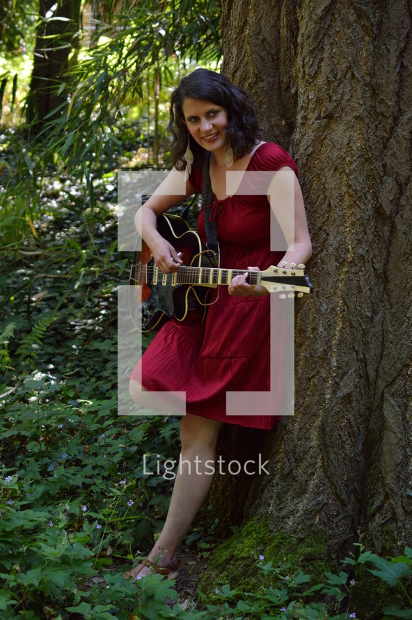 woman standing under a tree with a guitar 