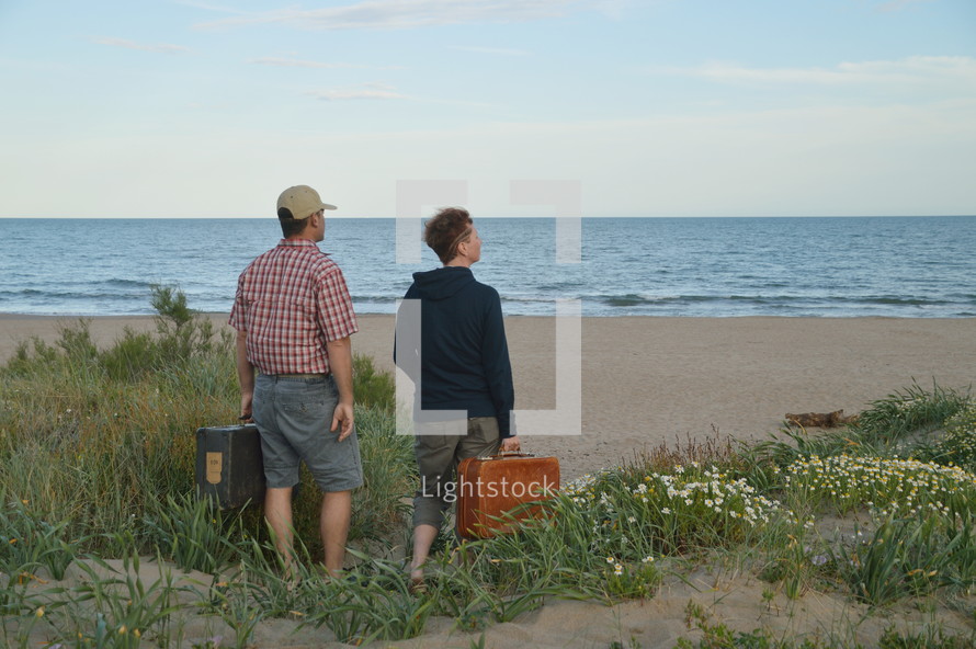man and woman with luggage walking towards a beach 