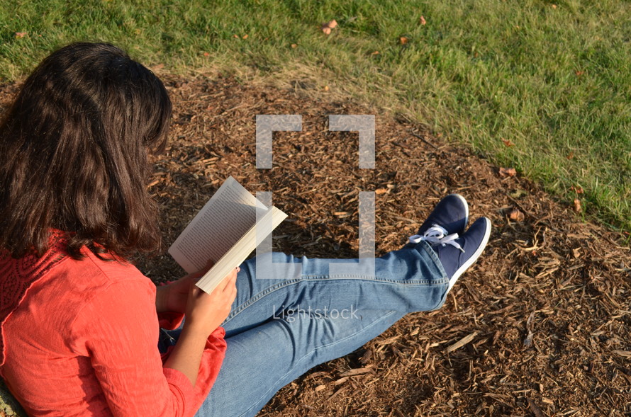 a young woman sitting on the ground reading a book 