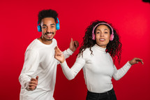 Young african american couple dancing with headphones isolated on red background studio. Party, happiness, music concept