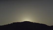 sun rising from behind a hill 