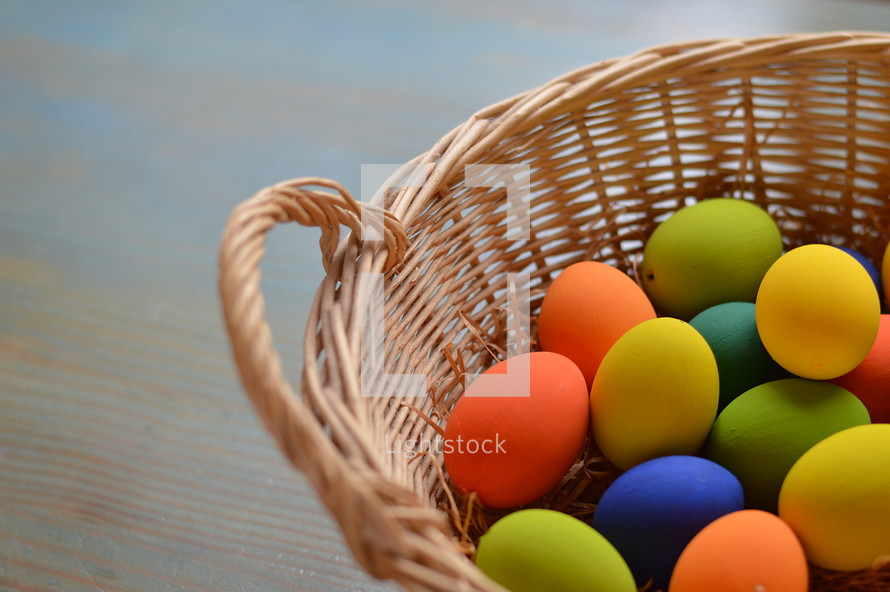 Colorfully painted Easter eggs on straw in a basket on a wooden table