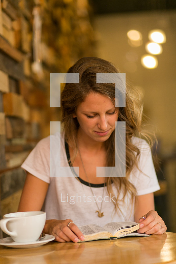 woman sitting at a table in a cafe reading a Bible