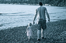 father and daughter holding hands walking on a rocky beach 
