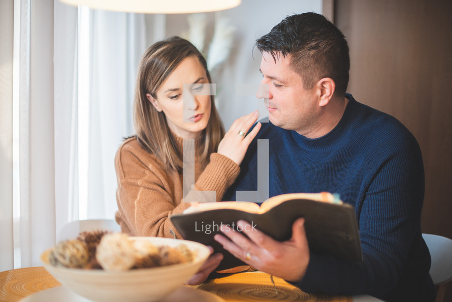 husband and wife reading a Bible together holding hands 