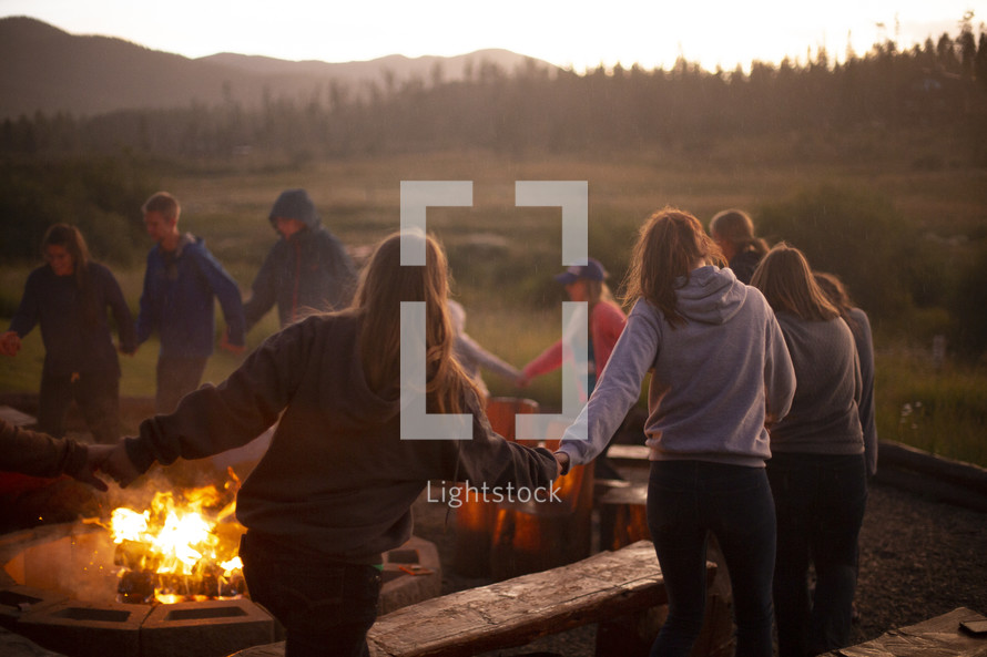 teens holding hands around a bonfire 