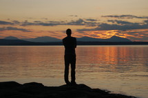 a silhouette of a man standing by lake water 