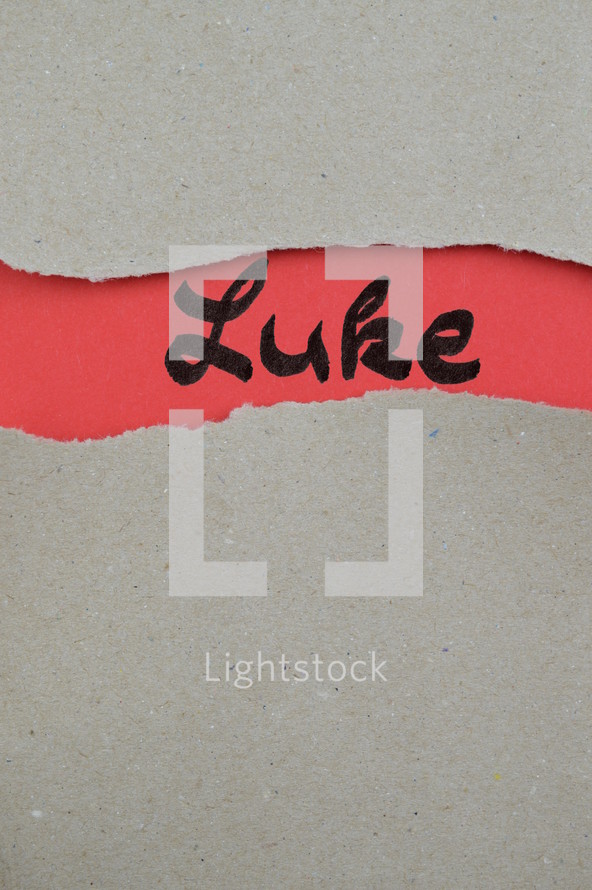 Luke - torn open kraft paper over light red paper with the name of the Gospel of Luke