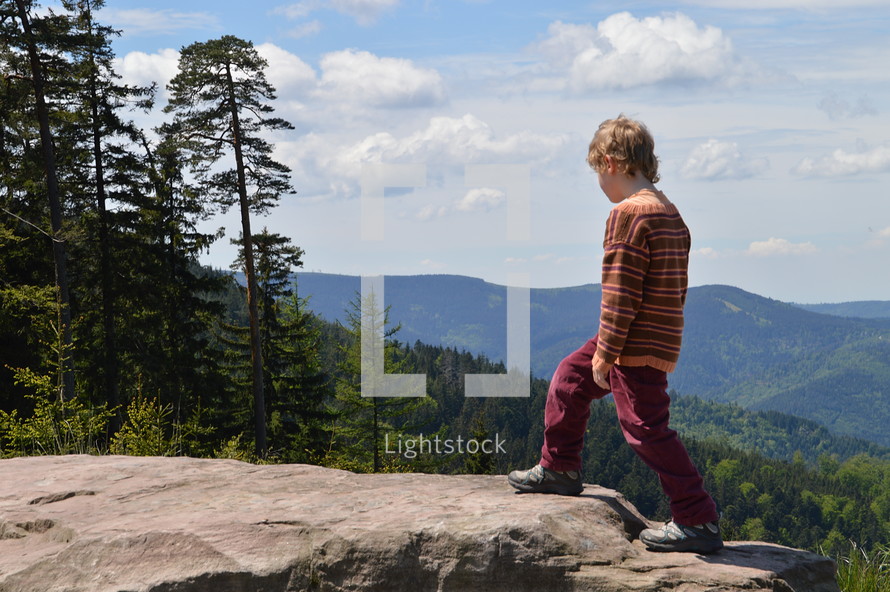 a child climbing to the top of a rock on a mountaintop 