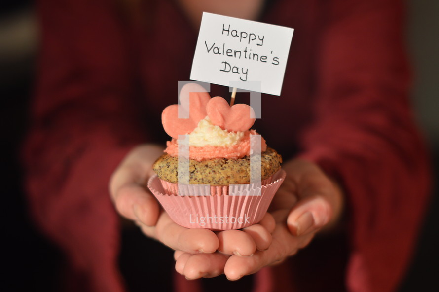Woman offering a cupcake with pink hearts and a sign saying HAPPY VALENTINE'S DAY. 