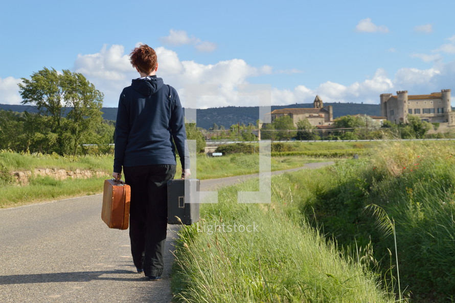 a woman walking carrying luggage on a rural road 