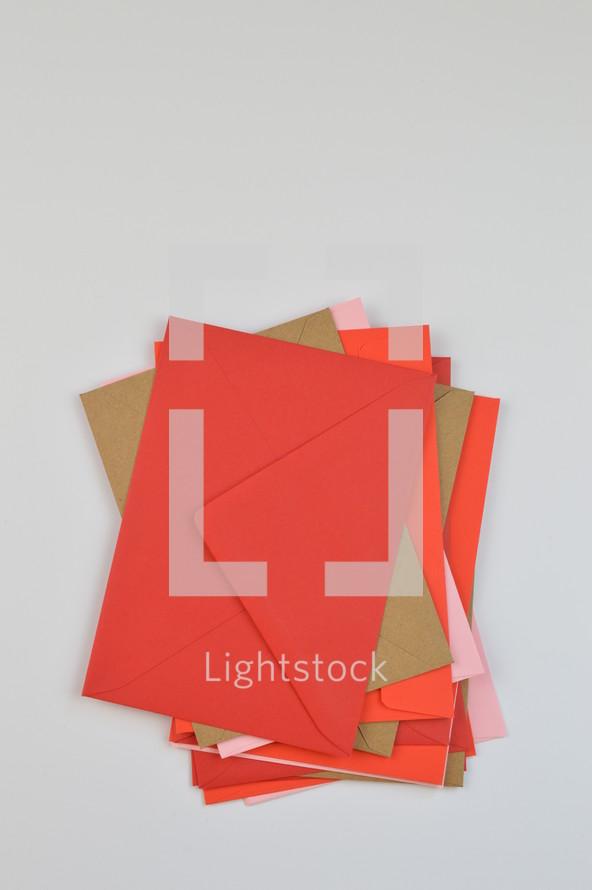 stacked envelopes - pile of red, pink and brown envelopes on white background with copy space above