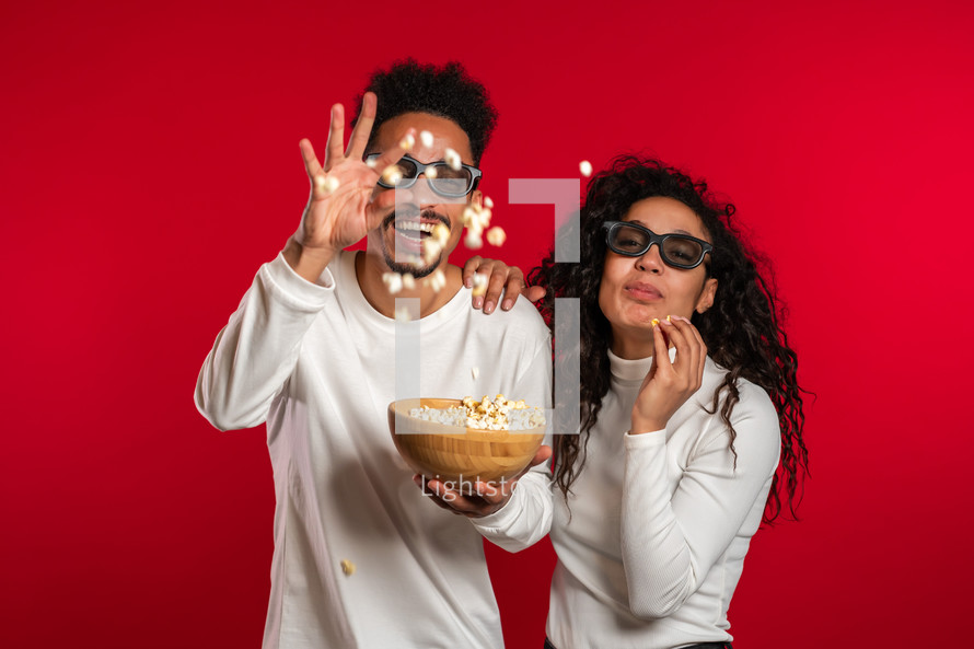 Young couple in cinema in 3d glasses watching comedy movie eating popcorn