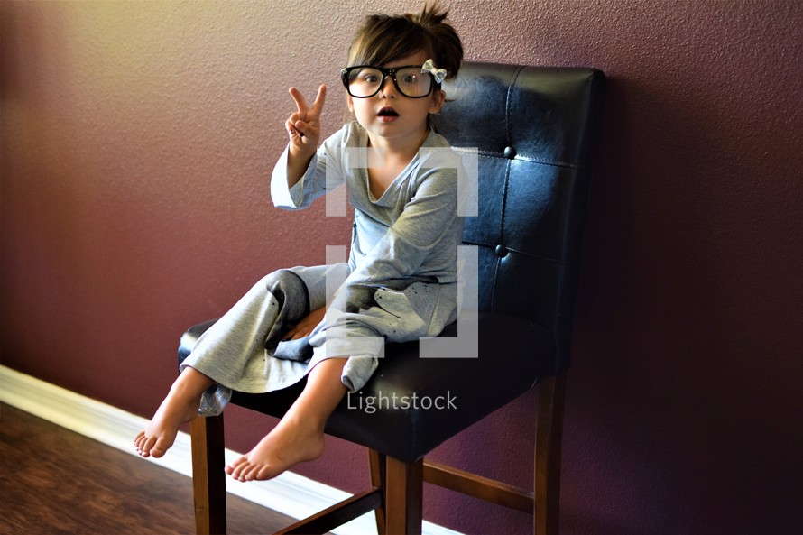 a little girl in glasses showing a peace sign 