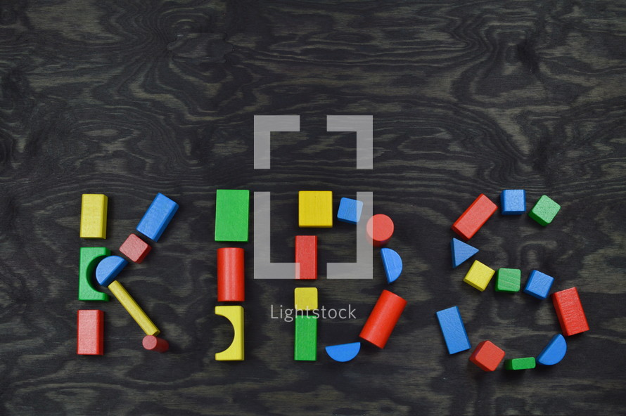 the word KIDS out of colorful wooden toy blocks on black wooden background