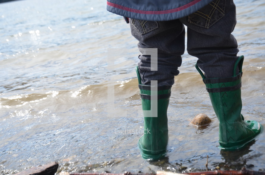 child in rain boots near water 