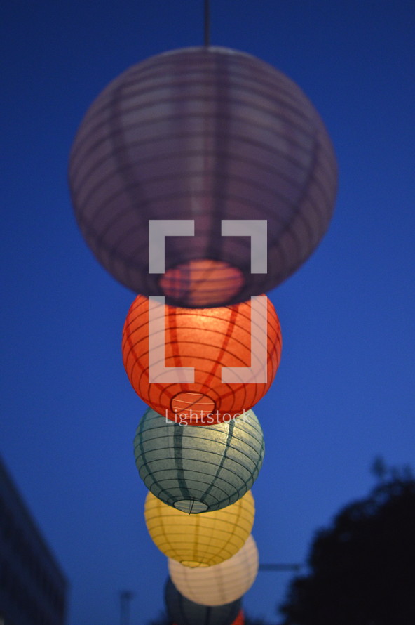 A string of colorful paper lanterns against a dusky blue sky.