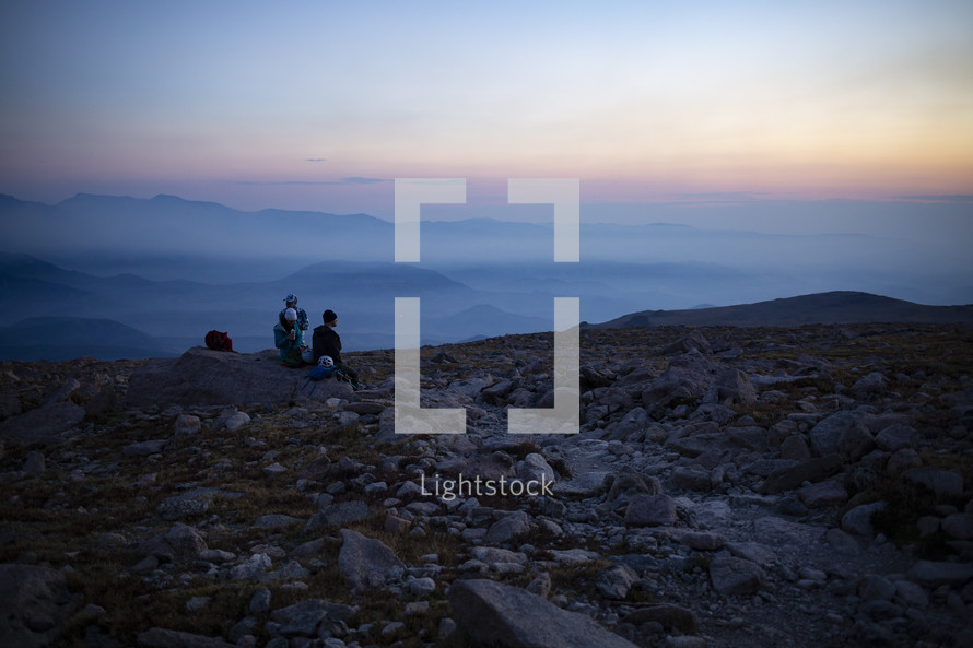 group sitting on a mountaintop watching the sunrise 