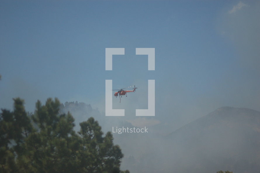 a helicopter with buckets flying over a forest fire 