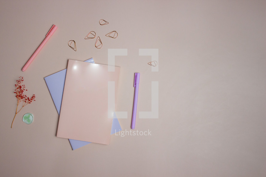 Notebook with pens, flowers, and office supplies on pink background