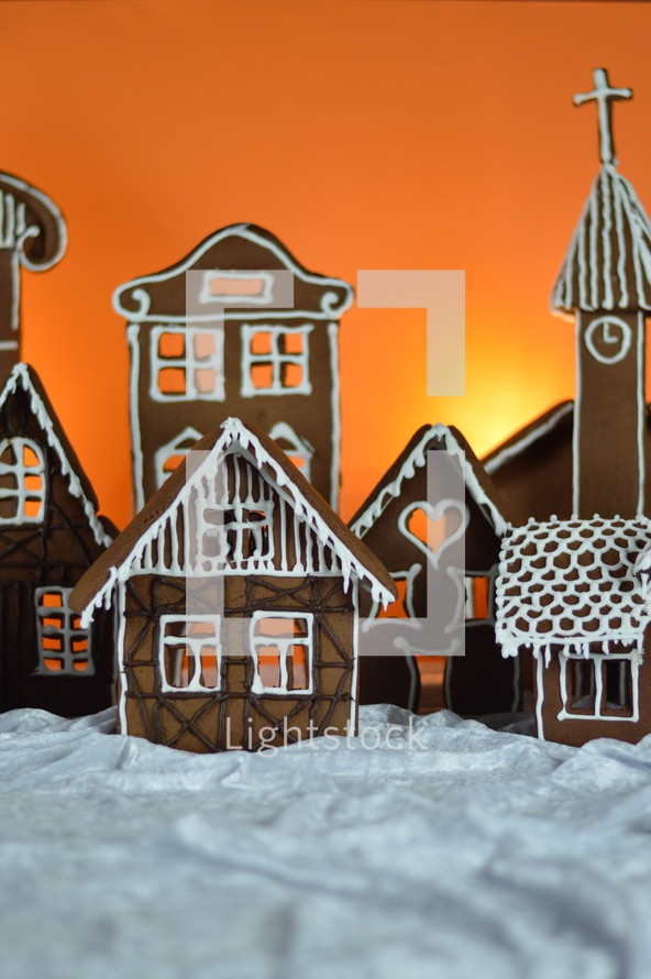 home made gingerbread village in front of orange background on white snowlike velvet as advent decoration
