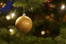 gold glittery Christmas ornament hanging from a Christmas tree 