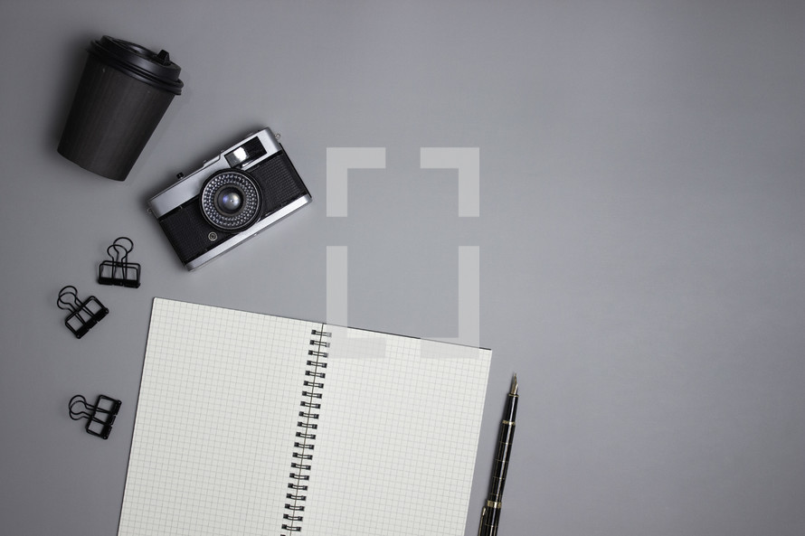 Cup, notebook, camera and office supplies on gray background
