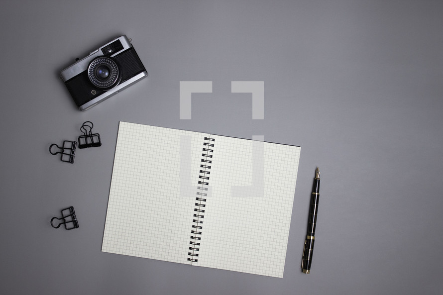 Camera with notebook and office supplies on gray background