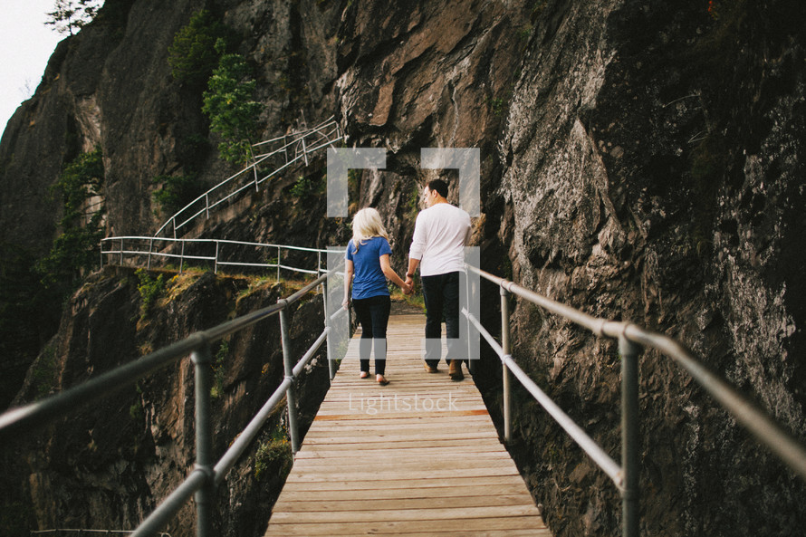 couple walking holding hands on mountain walking bridge