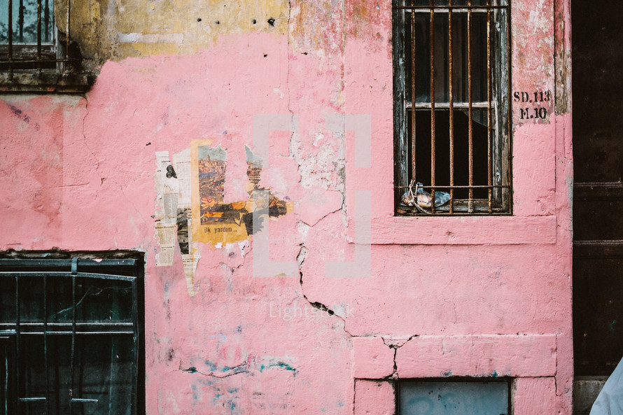 Barred windows and pealing paint on a pink wall. 