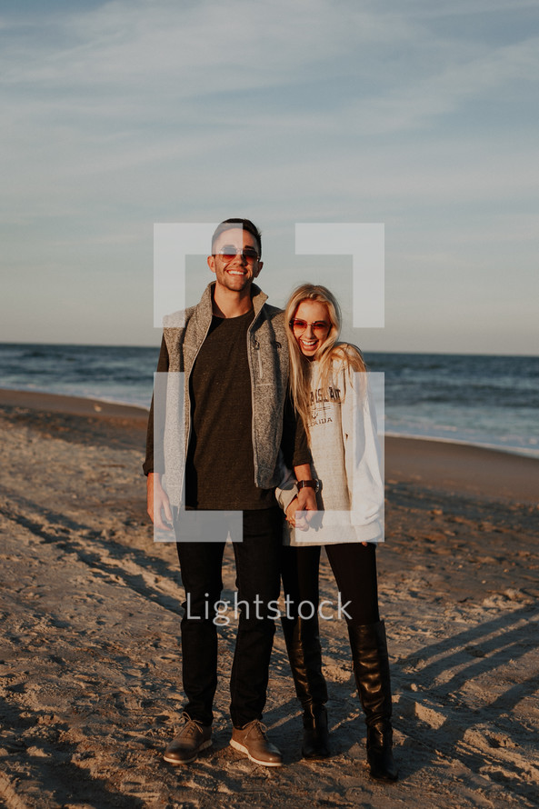 a couple standing on a beach holding hands 
