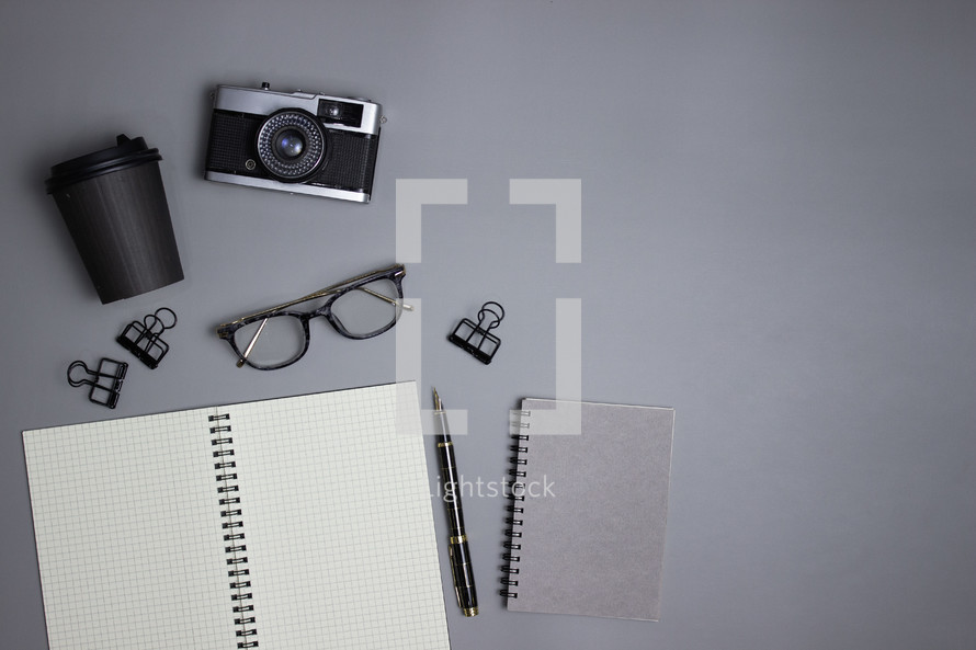 Notebook with camera, glasses, cup, and office supplies on gray background