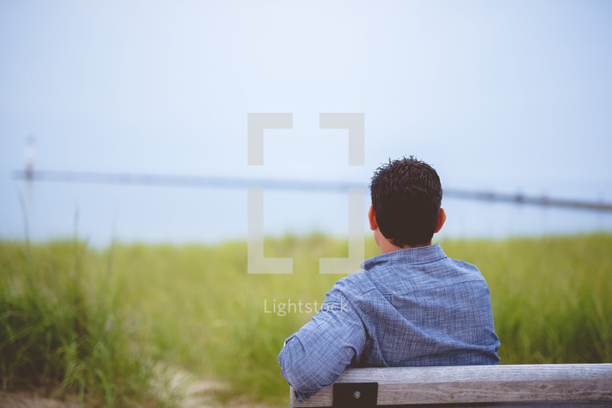 a man sitting on a bench looking out at the ocean 